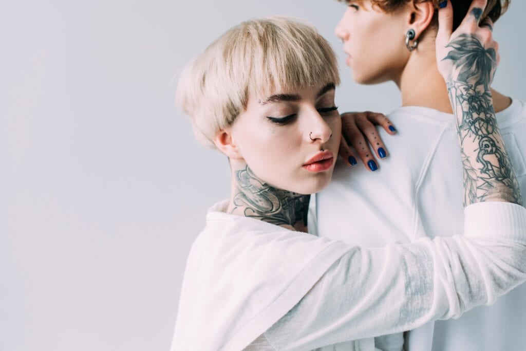 blonde girl with tattoos touching handsome boyfriend isolated on grey