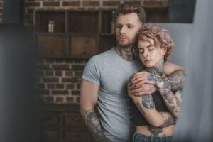 tender tattooed couple hugging in kitchen