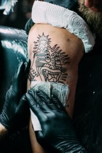 partial view of tattoo artist in gloves working on tattoo on shoulder in salon